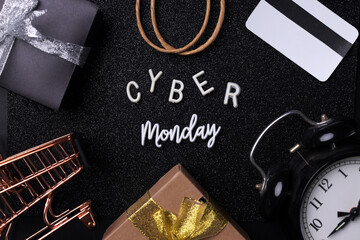 Cyber monday concept. Cyber monday word surrounded by credit card, gift boxes, alarm clock, paper bag and mini trolley isolated on black background. 