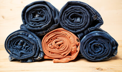Jeans are rolled up and stacked, on a wooden background. 