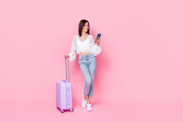 Full length photo of charming young girl luggage hold device search hotel dressed stylish white outfit isolated on pink color background