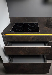 Induction cooker black glass hob or aspirating induction hob on marble stoneware countertop with horizontal sliding pull out drawer shelves storage in kitchen cupboard.