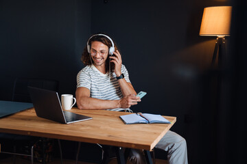Young man using laptop and headphones while sitting by desk in office