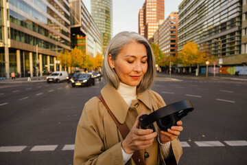 Mature asian woman using headphones while strolling on city street