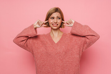 Young woman blocking her ears with irritation isolated over pink background