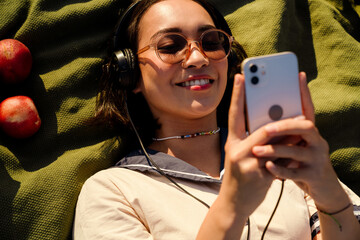 Top view of asian girl listening music with headphones and mobile phone while laying on blanket