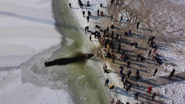 the drone flies over the hole in the winter rake, the river is covered with ice, people enter the cold water, cross themselves and plunge headlong into the ice water three times
