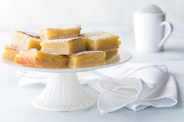 Lemon bars piled on a dessert stand with powdered sugar in behind.