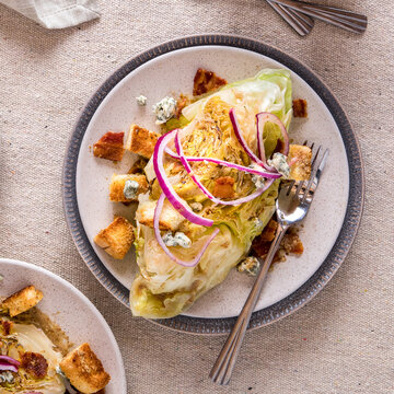 A Serving Of Warm Wedge Salad Garnished With Croutons, Red Onion And Bacon.