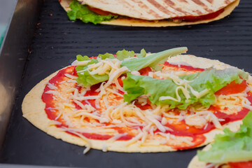 Preparing fresh quesadilla on black grill at summer local food market - close up view. Outdoor cooking, barbecue, gastronomy, cookery, street food and traditional Mexican dish concept