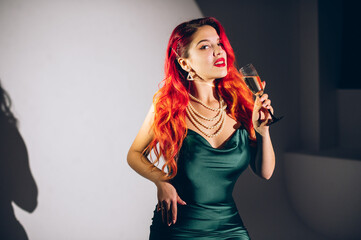 Naklejka premium Glamour red haired woman holding a glass of champagne on the contrast background