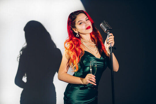 Glamour red haired lady singing with microphone on the dark stage background