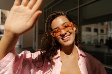 Positive young caucasian woman looking at camera smiling shaking hand outside. Model with brunette...