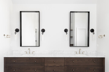 A luxury bathroom with a dark wood cabinet, marble countertop, and sconce lights around the square mirrors.