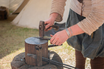 Professional blacksmith hand holding hammer, working with metal on anvil at outdoor workshop - close up view. Handmade, reenactment, craftsmanship, medival concept