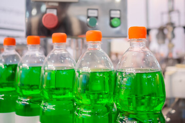 Row of pet bottles with green lemonade and orange caps on conveyor belt of automatic liquid filling machine at plastic exhibition - close up. Manufacturing, industry and technology equipment concept