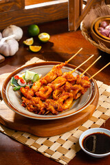Squid satay or squid skewer  with indonesian sambal serve on brown plate.
