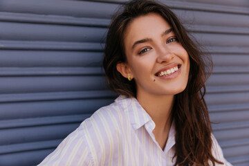 Close-up cheerful young caucasian girl smiling in camera spends time outdoor. Woman with brunette hair wears white shirt. Concept of leisure.