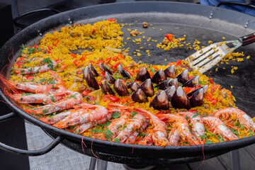 Cooked paella with shrimp, mussel, rice, spice, saffron in huge paella pan at summer outdoor food market: close up. Spanish cuisine, seafood, gastronomy, street food concept