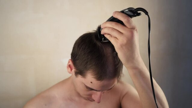 A handsome man personally cuts his hair with a machine trimmer, clipper at home. Self-service during quarantine isolation. Stay home, hairdresser.