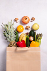 Fresh fruit and vegetables in paper bag on light gray background, top view, copy space