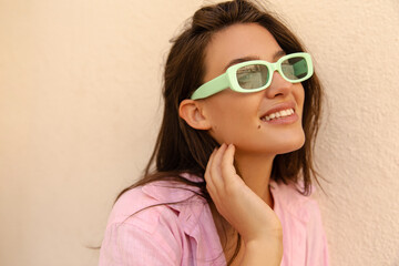 Close-up of pretty young caucasian model looking at distance smiling spends free time outdoor. Brunette wears pink shirt. Concept of stylish spring vacation.