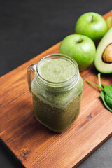 Green smoothie drink blended in a glass jar, avocado, spinach leaves and apples at wooden board