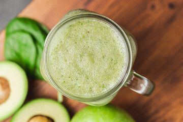 Green smoothie drink blended in a glass jar, avocado, spinach leaves and apples at wooden board, top view