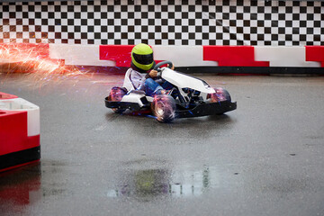 Child driving a real go-kart on a children's race track carefully bypasses an obstacle. Young karting racer trains at the circuit on wet asphalt after the rain - obrazy, fototapety, plakaty