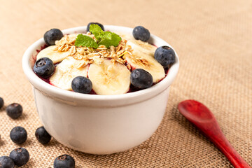 Acai bowl with banana, blueberry and cereal on burlap cloth.