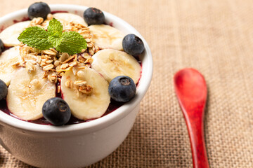 Acai bowl with banana, blueberry and cereal on burlap cloth.