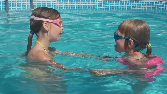 Two little girls are learning to dive underwater in a round pool 