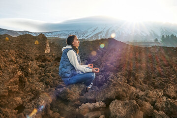 Happy tourist woman enjoying freedom while meditating on lava stone at panoramic view of snowy...