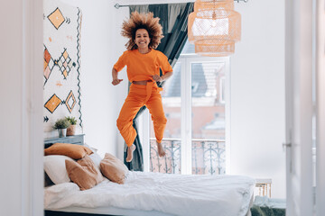 young african american woman dressing casual orange jumping for joy over bed