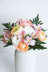 Beautiful bouquet of fresh colorful pastel ranunculus and lily flowers in full bloom with green fern leaves in vase against white background, close up. Spring bunch of buttercups.
