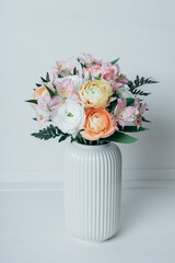 Beautiful bouquet of fresh colorful pastel ranunculus and lily flowers in full bloom with green fern leaves in vase against white background. Spring bunch of blossoms.