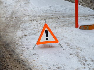 Warning triangle in the dirty snow on a winter street. Symbol for an accident on a slippery road. Danger signal for other road users to dive slowly and pay attention. Cold season in Europe.