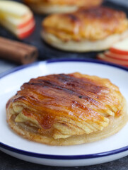 Pieces of a classic traditional mini French apple tart thin (tarte fine aux pommes) with its sliced fruit, cinnamon in background. It made with butter puff pastry pie, caramelized with brown sugar.
