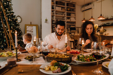 Happy family having dinner at table near Christmas tree