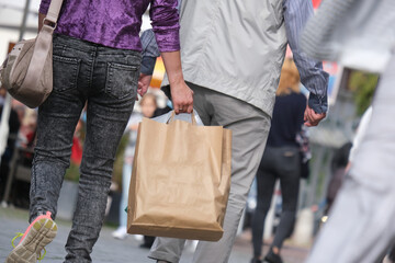 Junge Frau und älterer Herr sowie weitere Personen beim Shopping in einer Einkaufsstraße oder Fußgängerzone mit Einkaufstüten, selektiver Fokus