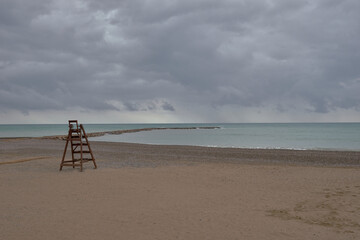 Fototapeta na wymiar Wooden lifeguard chair on lonely beach. Cloudy sky