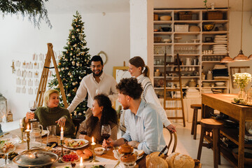 Group of joyful friends having traditional dinner together during Christmas holidays