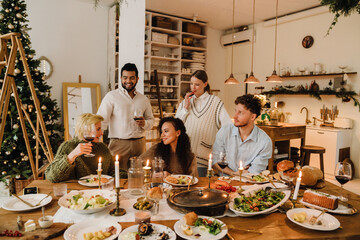 Group of joyful friends having traditional dinner together during Christmas holidays