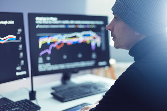 Side View Of Hipster Man Wearing Cap Following Stock Market Data At Office, Looking At Two Screens With Attentive Look, Cryptocurrency Investment From Home By Computer.