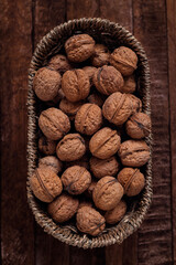 Organic whole walnuts in a oval wicker basket on a dark wooden background.