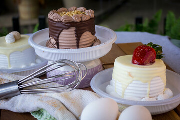mini chocolate, strawberry and cream cake, placed on a table with eggs, paste, wooden spoon, cake beater, with a rustic wooden base