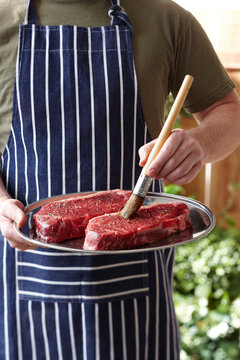 Man Brushing Steaks with Olive Oil