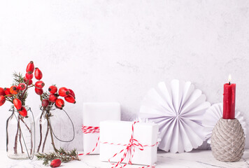Wrapped boxes with presents, briar berries in bottle, paper, rosettes, burning red candle against textured  wall. Scandinavian style. Place for text.