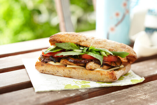 Grilled Chicken and Portobello Mushroom Sandwich on Whole Wheat Focaccia Bread with Basil, Tomato, and Cheese on Patio Table Outdoors, Canada