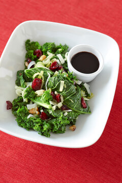 Kale Salad with Cranberries, Walnuts, Green Onions and Balsamic Dressing, on Red Background