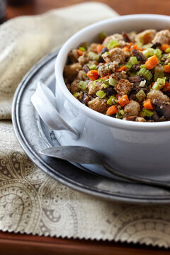 A large white ceramic serving bowl of holiday turkey stuffing or thanksgiving dressing with whole wheat bread cubes, carrots, celery, fresh rosemary, green onions, and seasoning. This is a family styl
