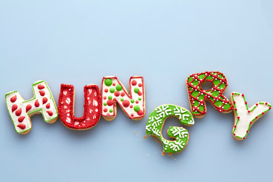 Overhead View of Christmas Sugar Cookies spelling HUNGRY with Bite out of one on Blue Background